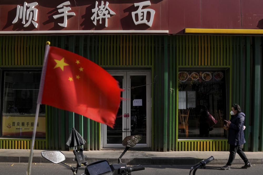 زنی با ماسک از کنار پرچم چین از جلوی رستوران نودل عبور می کند